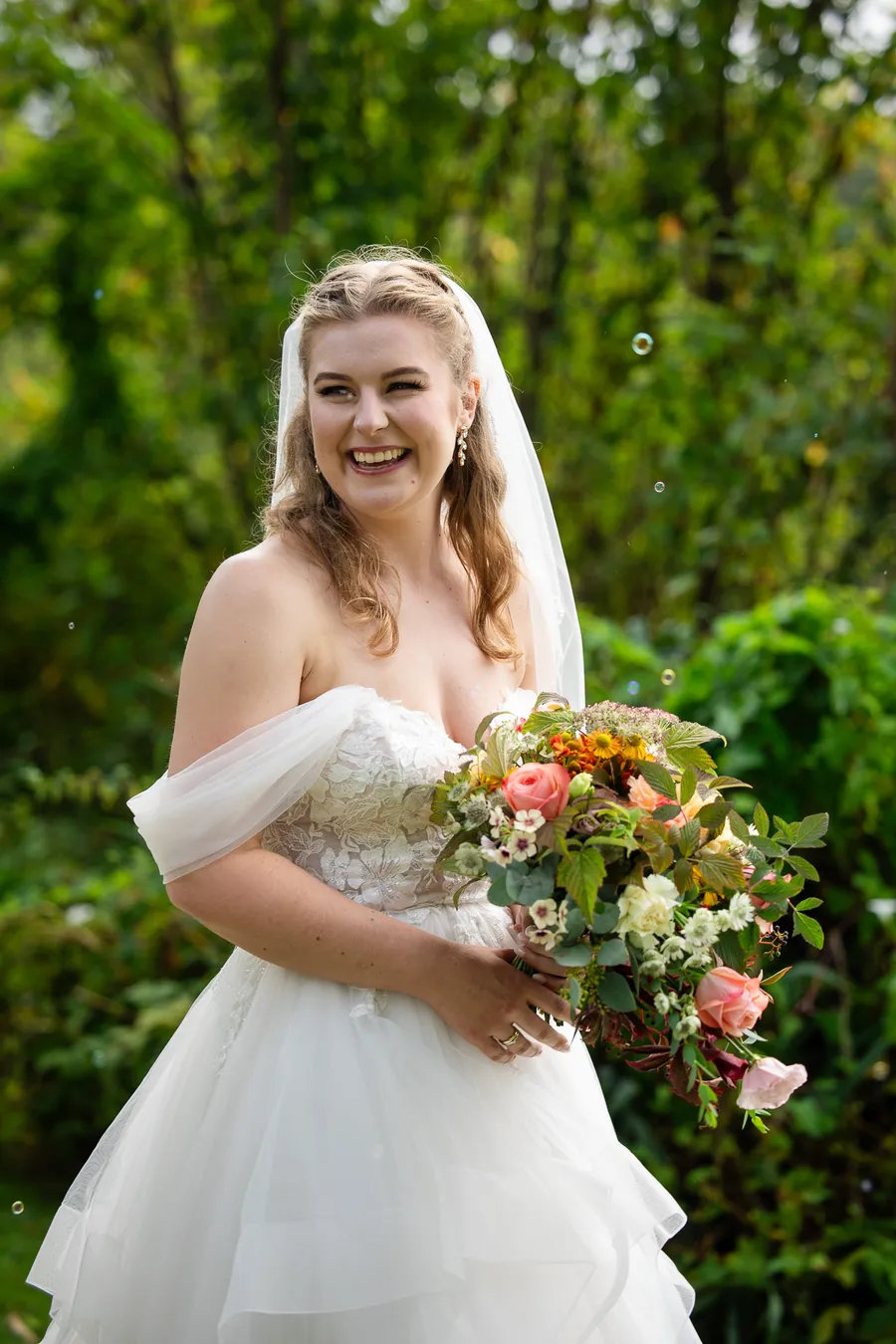 Bruden Turid ler med bukett av oransje roser, zinnia og tistler — bryllup på Tromøy