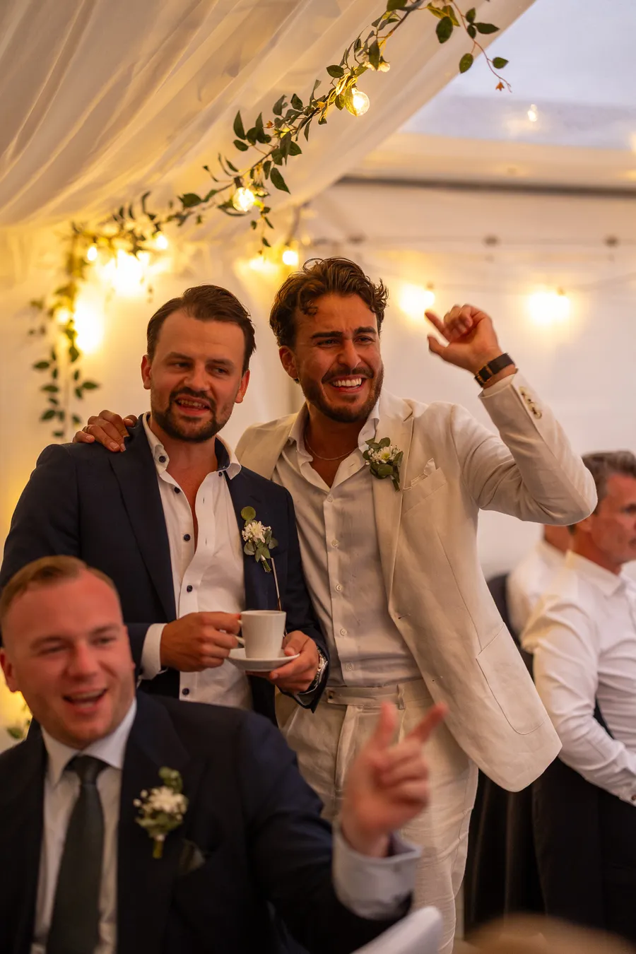 Forlovere ler og jubler i bryllupstelt med kaffekopp og corsage