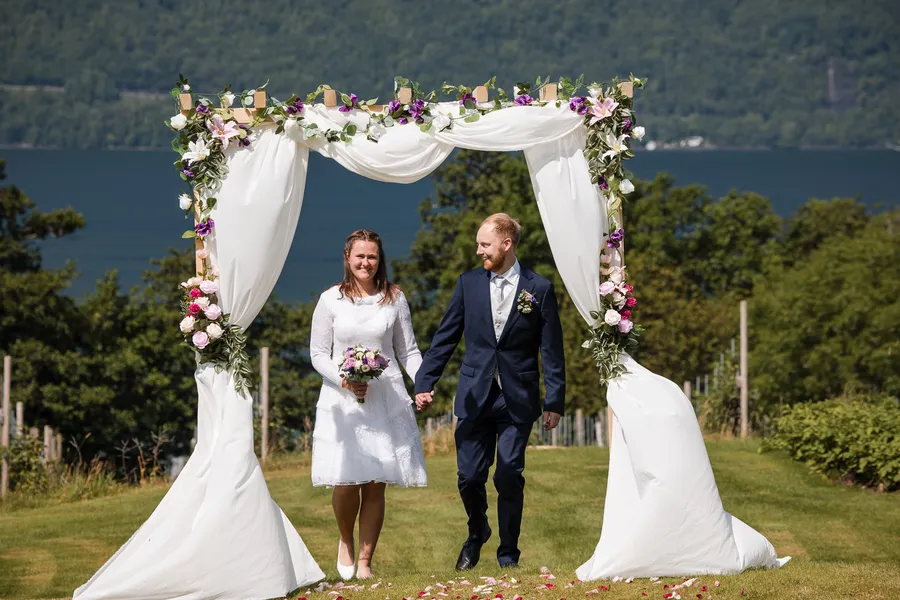 Brudeparet sammen under blomsterbuen ved fjorden