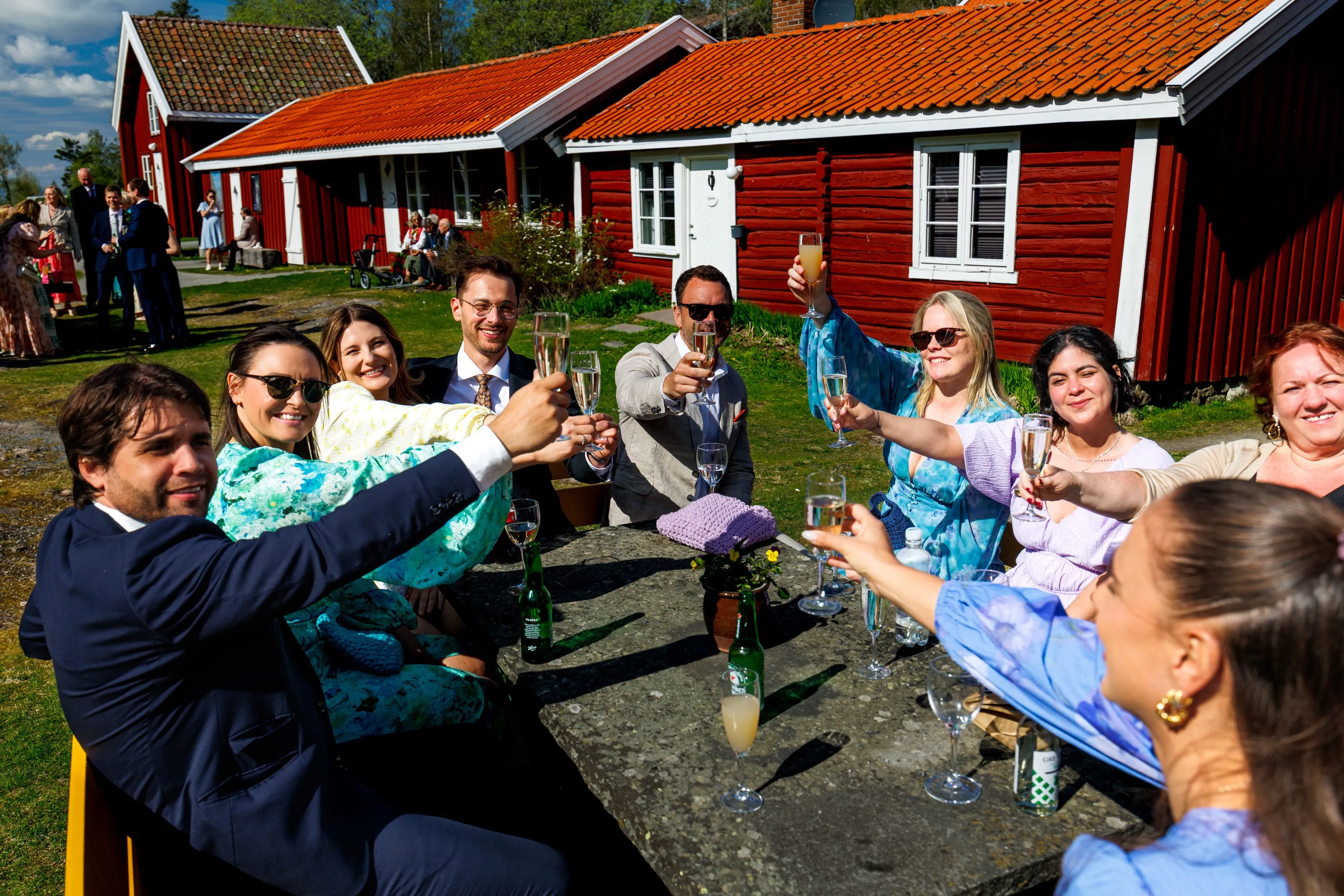 Sara og Knut Håkon skåler med bryllupsfølget utenfor de røde tømmerstuene på Kleivstua — bryllupsfotograf