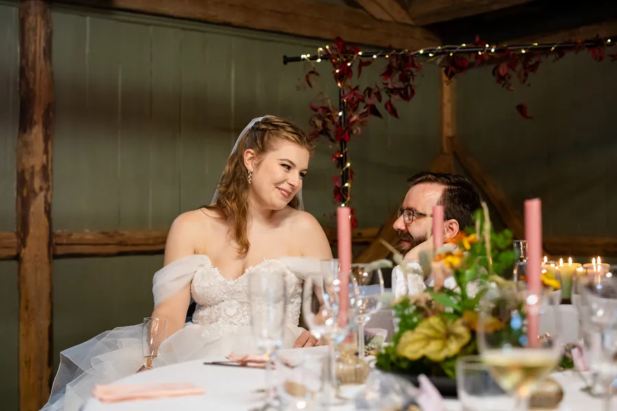 Brudepar sitter ved hovedbordet med stearinlys og høstblomster i låve