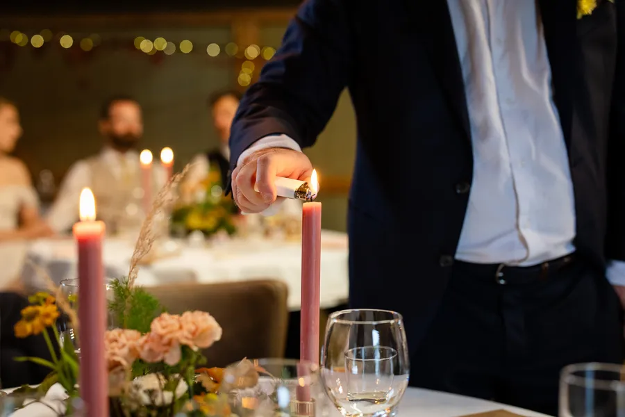 Detaljbilde av at noen tenner stearinlys ved bryllupsmiddag, varm stemning
